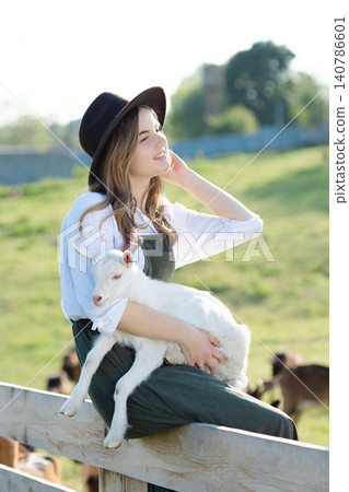 Young farmer woman holding a baby goat in a farm Young farmer woman holding a baby goat in a farm 140786601