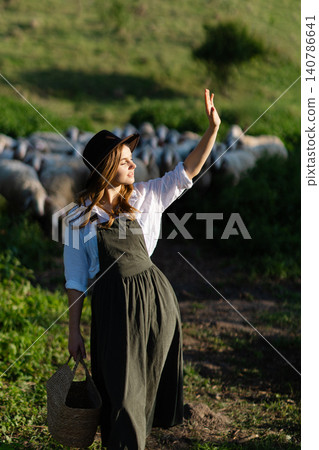 Shepherdess waving hand holding wicker basket walking on meadow with sheep flock in background Shepherdess waving hand holding wicker basket walking on meadow with sheep flock in background 140786641