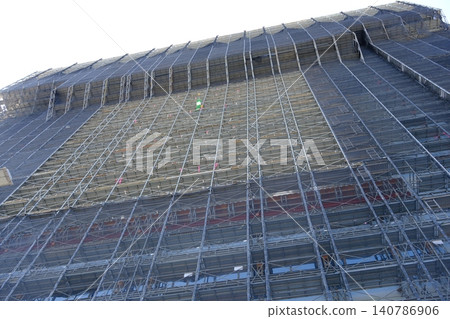 A massive construction site towering against the blue sky, with gigantic scaffolding neatly assembled. 140786906