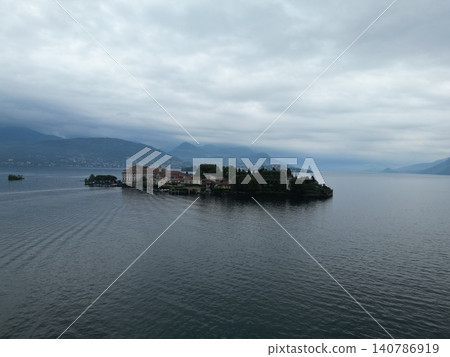 Island with red-roofed buildings floats on calm lake waters 140786919