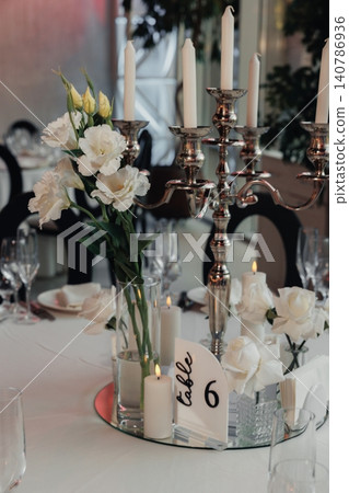 Elegant white roses bloom beside silver candle holders Elegant white roses bloom beside silver candle holders 140786936