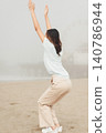 Woman stretches arms upward on sandy beach 140786944