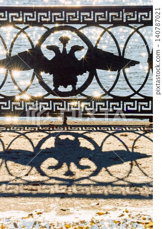 picturesque metal railings with a double-headed eagle and the crown of the Russian Empire on embankment in St. Petersburg, Russia, walking people, sunny autumn day, incredible sun glare Russia 140787021