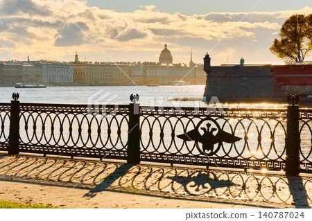 Isaac cathedral, Winter Palace, picturesque metal railings with a double-headed eagle and the crown of the Russian Empire on embankment in St. Petersburg, autumn sunset, incredible sun glare, Russia Isaac cathedral, Winter Palace, picturesque metal railings with a double-headed eagle and the crown of the Russian Empire on embankment in St. Petersburg, autumn sunset, incredible sun glare, Russia 140787024