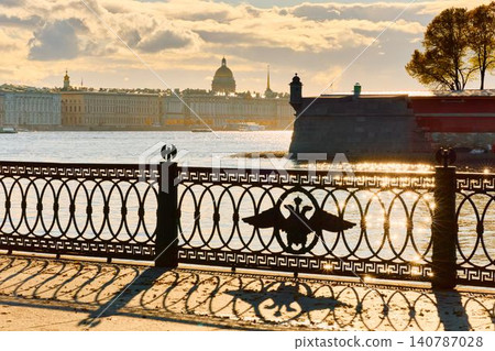 Isaac cathedral, Winter Palace, picturesque metal railings with a double-headed eagle and the crown of the Russian Empire on embankment in St. Petersburg, autumn sunset, incredible sun glare, Russia 140787028