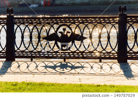 picturesque metal railings with a double-headed eagle and the crown of the Russian Empire on embankment in St. Petersburg, Russia, walking people, sunny autumn day, incredible sun glare Russia 140787029