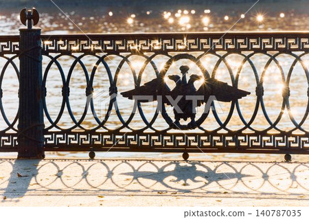 picturesque metal railings with a double-headed eagle and the crown of the Russian Empire on embankment in St. Petersburg, Russia, walking people, sunny autumn day, incredible sun glare Russia 140787035