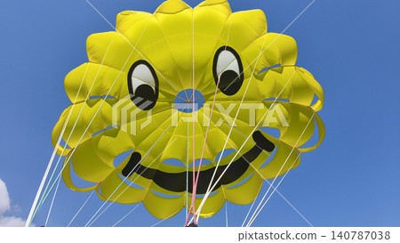 bright yellow smiley face parasailing canopy against a clear blue sky, fun, adventure and excitement of a sunny beach holiday and water sports activities. bright yellow smiley face parasailing canopy against a clear blue sky, fun, adventure and excitement of a sunny beach holiday and water sports activities. 140787038