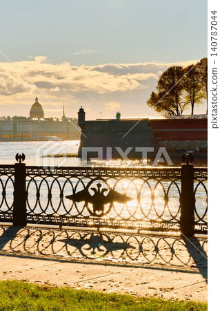 Isaac cathedral, Winter Palace, picturesque metal railings with a double-headed eagle and the crown of the Russian Empire on embankment in St. Petersburg, autumn sunset, incredible sun glare, Russia 140787044