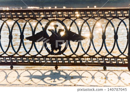 picturesque metal railings with a double-headed eagle and the crown of the Russian Empire on embankment in St. Petersburg, Russia, walking people, sunny autumn day, incredible sun glare Russia 140787045