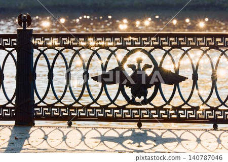 picturesque metal railings with a double-headed eagle and the crown of the Russian Empire on embankment in St. Petersburg, Russia, walking people, sunny autumn day, incredible sun glare Russia 140787046