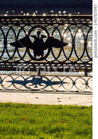 picturesque metal railings with a double-headed eagle and the crown of the Russian Empire on embankment in St. Petersburg, Russia, walking people, sunny autumn day, incredible sun glare Russia picturesque metal railings with a double-headed eagle and the crown of the Russian Empire on embankment in St. Petersburg, Russia, walking people, sunny autumn day, incredible sun glare Russia 140787047