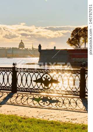Isaac cathedral, Winter Palace, picturesque metal railings with a double-headed eagle and the crown of the Russian Empire on embankment in St. Petersburg, autumn sunset, incredible sun glare, Russia Isaac cathedral, Winter Palace, picturesque metal railings with a double-headed eagle and the crown of the Russian Empire on embankment in St. Petersburg, autumn sunset, incredible sun glare, Russia 140787051
