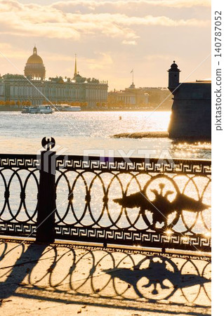 Isaac cathedral, Winter Palace, picturesque metal railings with a double-headed eagle and the crown of the Russian Empire on embankment in St. Petersburg, autumn sunset, incredible sun glare, Russia 140787052