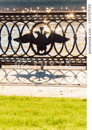 picturesque metal railings with a double-headed eagle and the crown of the Russian Empire on embankment in St. Petersburg, Russia, walking people, sunny autumn day, incredible sun glare Russia picturesque metal railings with a double-headed eagle and the crown of the Russian Empire on embankment in St. Petersburg, Russia, walking people, sunny autumn day, incredible sun glare Russia 140787056