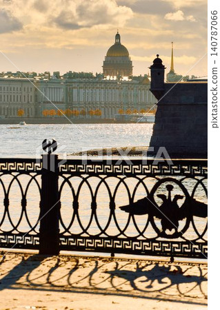 Isaac cathedral, Winter Palace, picturesque metal railings with a double-headed eagle and the crown of the Russian Empire on embankment in St. Petersburg, autumn sunset, incredible sun glare, Russia Isaac cathedral, Winter Palace, picturesque metal railings with a double-headed eagle and the crown of the Russian Empire on embankment in St. Petersburg, autumn sunset, incredible sun glare, Russia 140787066