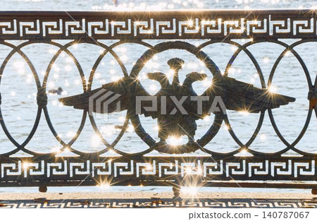 picturesque metal railings with a double-headed eagle and the crown of the Russian Empire on embankment in St. Petersburg, Russia, walking people, sunny autumn day, incredible sun glare Russia 140787067