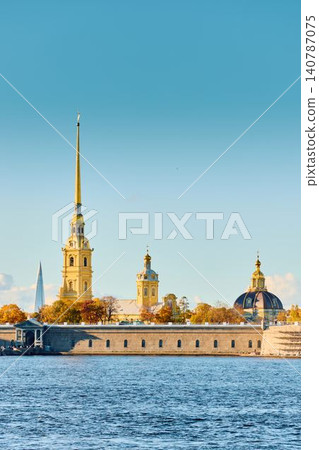 The golden spire of the Peter and Paul Fortress through yellow leaves in Saint-Petersburg - Russia at sunny autumn day, cross with angel on spire, red leaves, sunset, clear sky 140787075