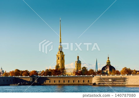The golden spire of the Peter and Paul Fortress through yellow leaves in Saint-Petersburg - Russia at sunny autumn day, cross with angel on spire, red leaves, sunset, clear sky 140787080