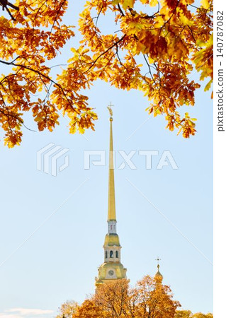 The golden spire of the Peter and Paul Fortress through yellow leaves in Saint-Petersburg - Russia at sunny autumn day, cross with angel on spire, red leaves, sunset, clear sky The golden spire of the Peter and Paul Fortress through yellow leaves in Saint-Petersburg - Russia at sunny autumn day, cross with angel on spire, red leaves, sunset, clear sky 140787082