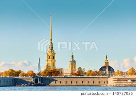 The golden spire of the Peter and Paul Fortress through yellow leaves in Saint-Petersburg - Russia at sunny autumn day, cross with angel on spire, red leaves, sunset, clear sky 140787086