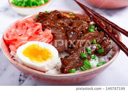 Gyudon Japanese beef with rice, pickled ginger, boiled egg slice, garnished with green onions, in a bowl with chopsticks, Gyudon Japanese beef with rice, pickled ginger, boiled egg slice, garnished with green onions, in a bowl with chopsticks, 140787199