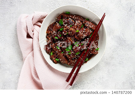 Crispy beef, with green onions and sesame seeds, in a bowl with chopsticks, on a textured surface, on a light background, no people Crispy beef, with green onions and sesame seeds, in a bowl with chopsticks, on a textured surface, on a light background, no people 140787200