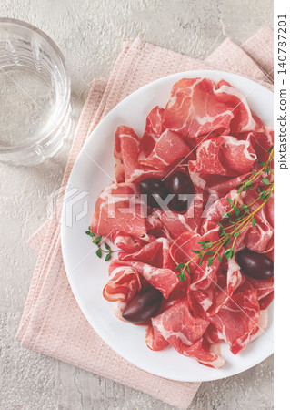 Freshly cut dried meat, served with olives and herbs, on a white plate, light background, no people, Freshly cut dried meat, served with olives and herbs, on a white plate, light background, no people, 140787201