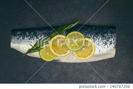 Fresh fish fillet, garnished with lemon and herbs, on a dark background, ready to cook Fresh fish fillet, garnished with lemon and herbs, on a dark background, ready to cook 140787208