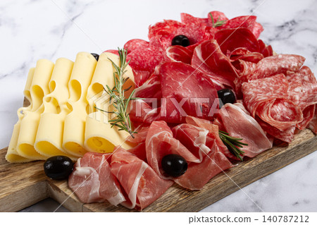 Assorted meat, appetizer, prosciutto, salami and ham, with maasdam cheese and olives, on a wooden board, breakfast, top view, close-up, no people Assorted meat, appetizer, prosciutto, salami and ham, with maasdam cheese and olives, on a wooden board, breakfast, top view, close-up, no people 140787212
