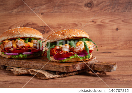 two shrimp burgers and buns with sesame seeds, bacon, lettuce, tomatoes and onions,on a wooden board, rustic style, 140787215