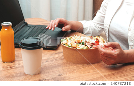 a woman is working on a laptop at home, there is food on the table, salad, coffee and juice, delivery, a woman is working on a laptop at home, there is food on the table, salad, coffee and juice, delivery, 140787218