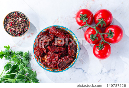 Dried tomatoes, in a bowl with fresh herbs and spices, on a white marble surface, no people 140787226