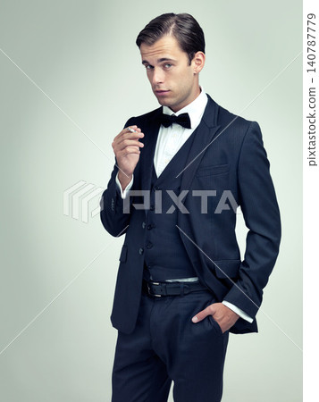 Portrait, attitude or young gentleman smoking a cigarette in studio, confidence or vintage fashion by white background. Face, serious or man in retro suit or tuxedo, bow tie or classy at formal event Portrait, attitude or young gentleman smoking a cigarette in studio, confidence or vintage fashion by white background. Face, serious or man in retro suit or tuxedo, bow tie or classy at formal event 140787779