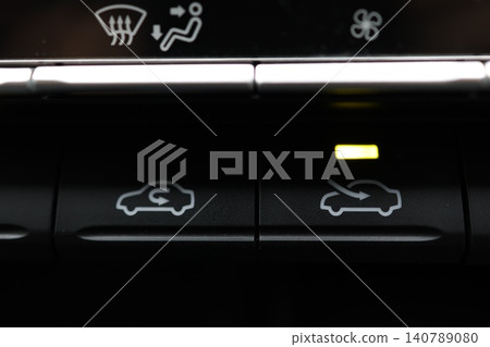 The car's air conditioning's outside air intake button is illuminated with a yellow light. The car's air conditioning's outside air intake button is illuminated with a yellow light. 140789080