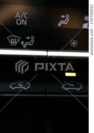 The car's air conditioning's outside air intake button is illuminated with a yellow light. The car's air conditioning's outside air intake button is illuminated with a yellow light. 140789082