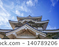 A traditional Japanese castle tower stands out against the blue sky. A powerful view of the castle architecture from a low angle. (Tourist image) 140789206