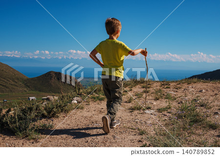 Boy hiker with stick walks on a mountain trail Boy hiker with stick walks on a mountain trail 140789852