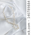 An image of a pearl necklace placed on a white cloth. 140789884