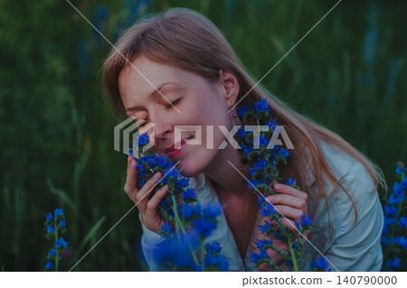 Portrait of young woman with blue flowers in a field Portrait of young woman with blue flowers in a field 140790000