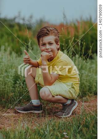 Happy boy sits in green meadow and gives a thumbs up Happy boy sits in green meadow and gives a thumbs up 140790009