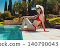 Beautiful woman in red swimsuit sitting by the pool at the resort 140790043