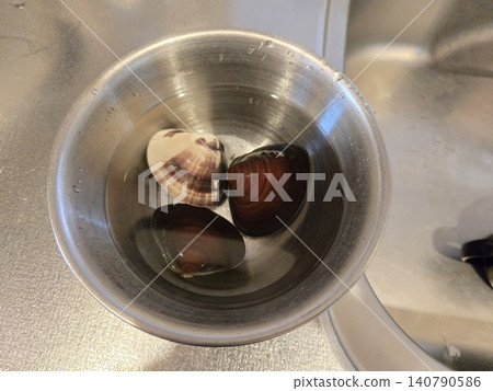 Freshly picked clams are soaked in a stainless steel bowl of water to remove the sand. Freshly picked clams are soaked in a stainless steel bowl of water to remove the sand. 140790586