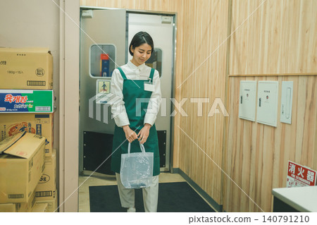 一名女店員拿著一個透明袋子站在旋轉門前。 140791210