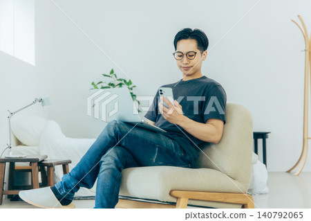 Man sitting on sofa and using smartphone Man sitting on sofa and using smartphone 140792065