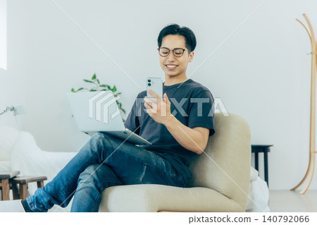 Man sitting on sofa and using smartphone Man sitting on sofa and using smartphone 140792066