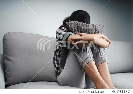 Girl sitting on sofa hugging her knees feeling sad Girl sitting on sofa hugging her knees feeling sad 140793327