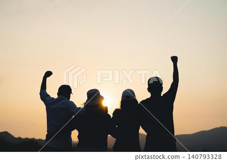 Group of four friends celebrating sunset outdoors with raised fists Group of four friends celebrating sunset outdoors with raised fists 140793328