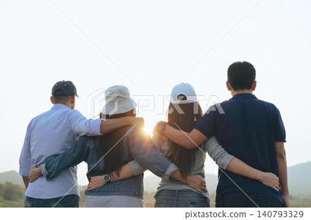 Group of four friends sitting together outdoors at sunset Group of four friends sitting together outdoors at sunset 140793329
