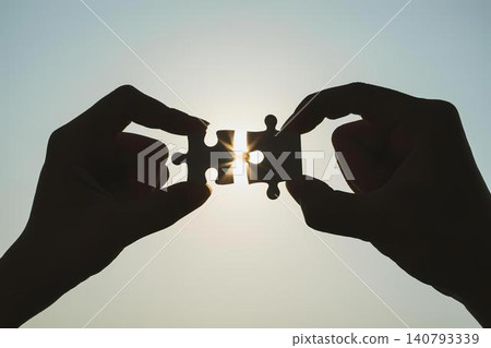 Hands holding puzzle pieces fitting together with sunlight Hands holding puzzle pieces fitting together with sunlight 140793339